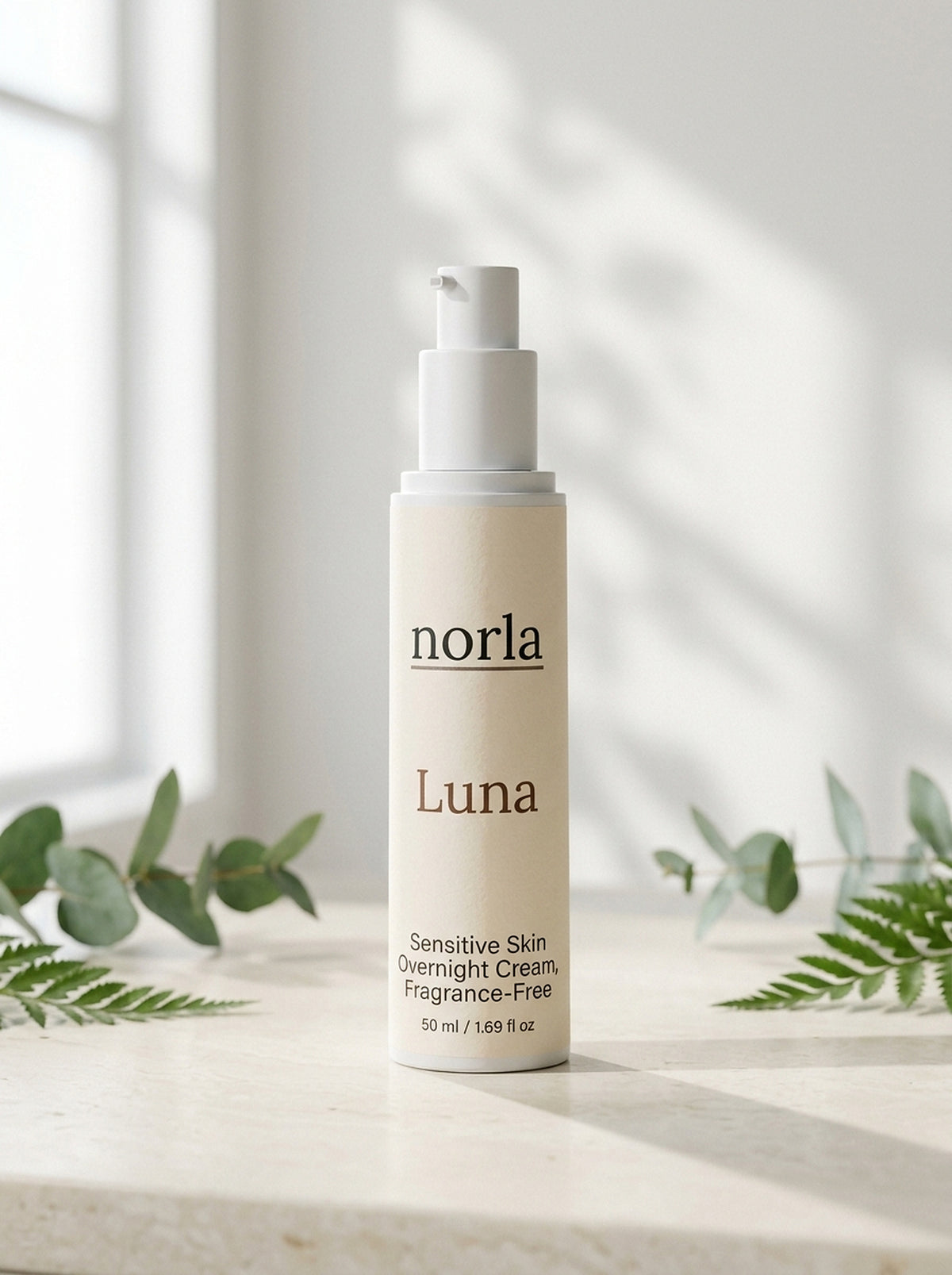 Luna Sensitive Skin Overnight Cream 50 ml by Norla, airless pump bottle on a marble surface with eucalyptus and fern