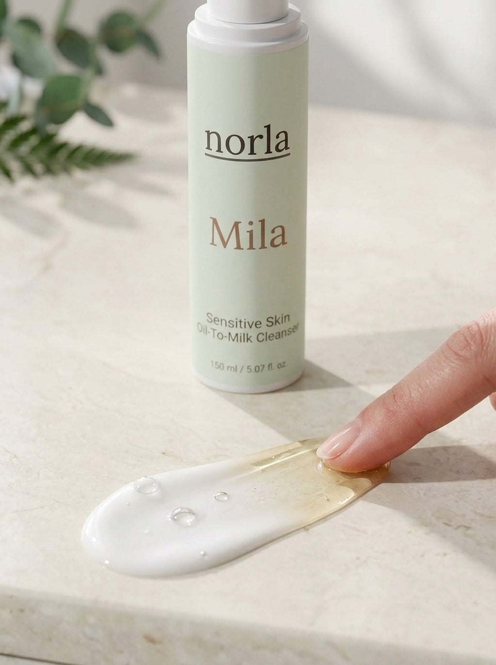 Texture of Mila Oil-To-Milk Cleanser by Norla: dewy oil-gel turning into a silky white milk next to the bottle