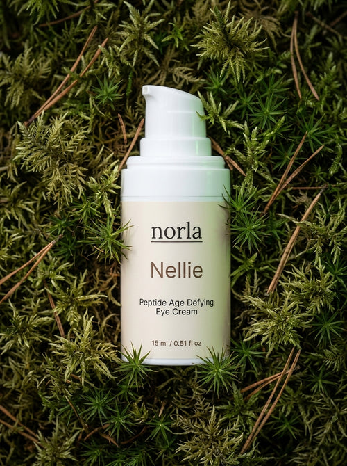 Nellie Peptide Age-Defying Eye Cream 15 ml by Norla, small airless pump bottle lying on green moss