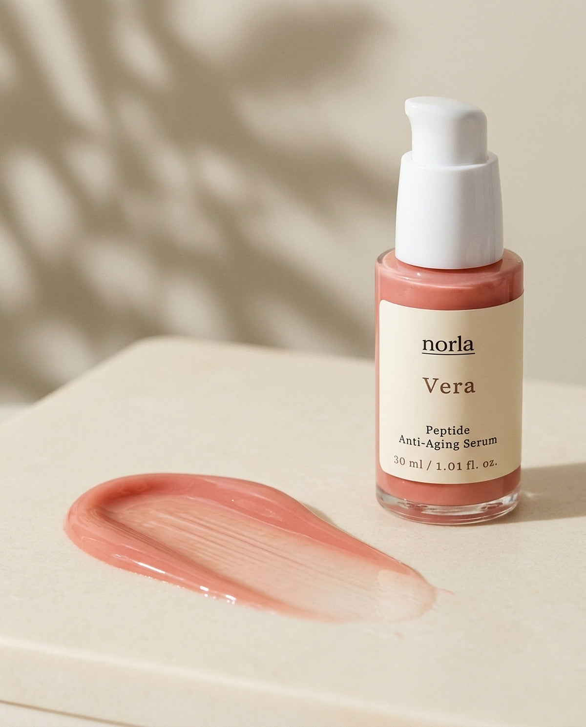 Texture of Vera Peptide Anti-Aging Serum by Norla: a lightweight rose-tinted serum smear next to the bottle